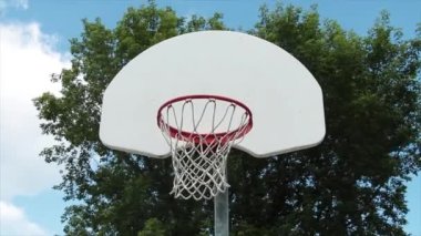 Açık hava basketbol ağının önünde beyaz arka tahtası ve arka planda ağaçtan ve gökyüzünden fışkıran gümüş direkle örülmüş.