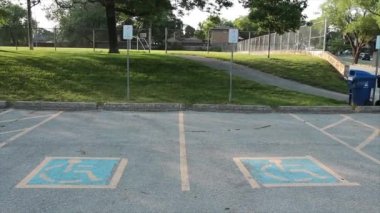 mavi ve sarı engelli logosu olan iki engelli park yeri, arkalarında küçük çim tepesi yolu ve futbol sahası.