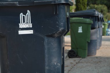 Toronto şehrinin uzun sıra geri dönüşümü ve kaldırımında logo olan yeşil çöp kutuları yerleşim yerindeki bir sokakta çöp kamyonu tarafından alınmak üzere.