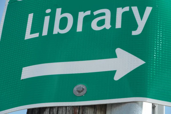 绿色背景白字图书馆金属标志 箭头指向木柱 — 图库照片