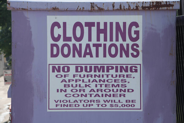 большая светло-фиолетовая металлическая корзина со знаком, гласящим, что пожертвования на одежду не будут сбрасывать мебель, бытовую технику, сыпучие предметы в контейнерах или вокруг них нарушители будут оштрафованы до $5000, при закрытии на знак