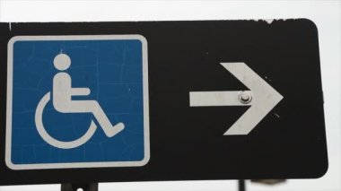 handikap işareti. Sağında beyaz ok olan mavi logo. Siyah dikdörtgen üzerinde yatay işaret.