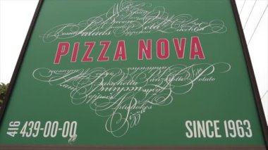 Pizzanın nova kare tabelası, yeşil arka planda kırmızı yazı, yukarıdaki ve aşağıdaki süslü sanat eserleri, telefon numarası 439 0000 ve 1963 'ten beri de üstünde, aşağıdan çekilen telefon numarası