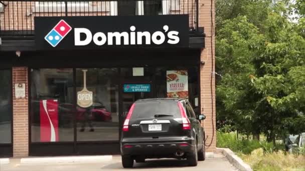 小さなドミノ ピザチェーン フランチャイズ レストラン フロントに車の駐車場と前を通る交通 店の右に木 — ストック動画