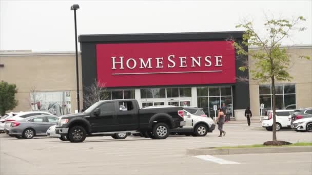 ホームセンスフロントエントランスサインロゴ 駐車場で前方に移動する人々 車のブロックショットで終わる 赤い背景に白い書き込み — ストック動画