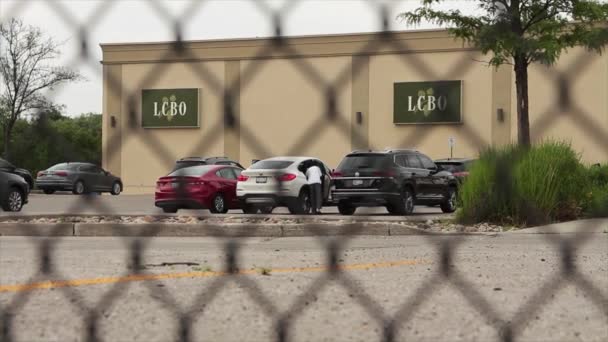 建物のオントリオのロゴの側面のLcboのアルコール コントロール ボード 車で得る車および人との駐車場 塀を通って撃ちました — ストック動画