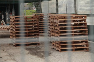 Ahşap palet yığınları, dışarıdaki tepe örtüsü çadırda kayıyor. Dikdörtgen metal çitin içinden plastik camlar, tahta rengi kaymalar, dar atış.