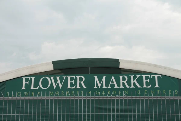 flower market flower markets garden centres caption sign at top of greenhouse with rectangle silver fence in front, white writing on green background