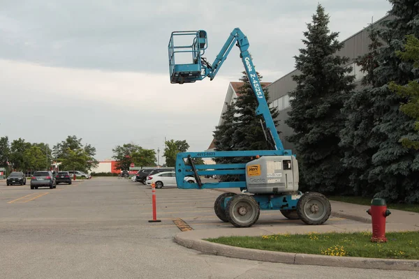 stock image herc rentals genie blue and gray crane parked in parking lot with large parking lot in background with some parked cars, next to a building, calm still background