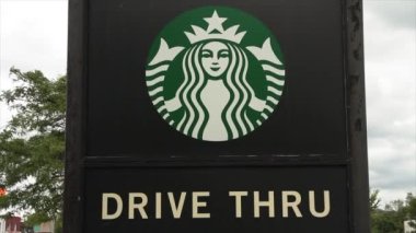 Starbucks logosu altında beyaz büyük harflerle siyah parçacık dikdörtgen üzerinde ağaçlar ve arka planda gökyüzü işareti olduğunu söylüyor.