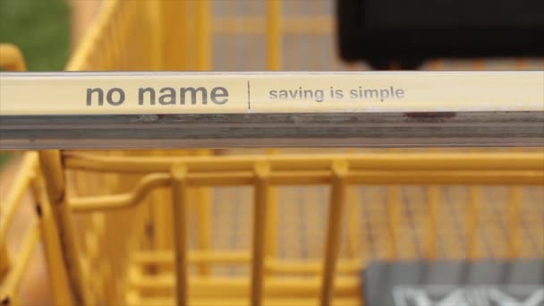 名前を節約しない黄色いショッピングカートは カートがぼやけていることに焦点を当ててハンドルに黒で書かれています — ストック動画