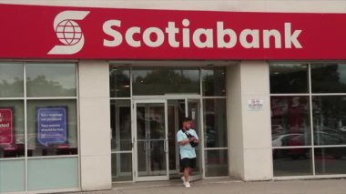 Scotiabank mağazası. Müşteri yaya çıkışı, otomobiller ve önünden geçen trafik, dükkanın girişinde pencereli metin logosu yazma, kırmızı arka planda beyaz yazı, kapat.
