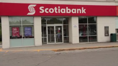 Scotiabank mağazası. Müşteri yaya çıkışı, otomobiller ve ön kapıdan geçen scooter, dükkânın girişinde pencereli metin logosu, kırmızı arka planda beyaz yazı