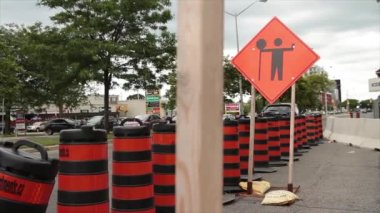 Elmas turuncu inşaat tabelasının üzerinde elinde dur işareti olan siyah baskı işareti, yoğun yolda iki yoldan da geçen trafik, ön merkez çerçevesinde ahşap direkler.