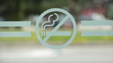 Camda sigara sembolü yok. Bulanık yayalar, geçen arabalar, yeşil ağaçlar ve arkasındaki yol.