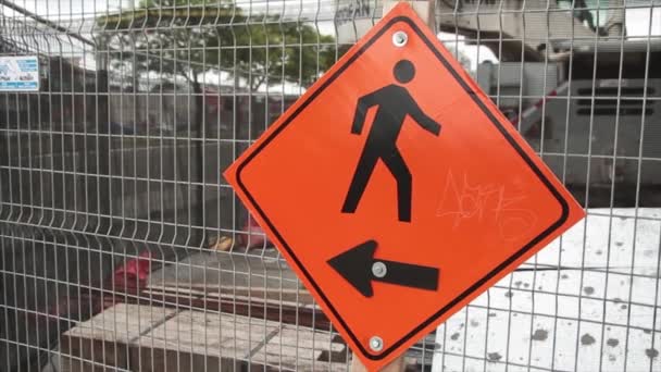 用箭头指向左边的菱形橙色标志 用黑色字体右行的人被固定在长方形银色栅栏上 封闭的建筑区域 交通通过框左边 — 图库视频影像