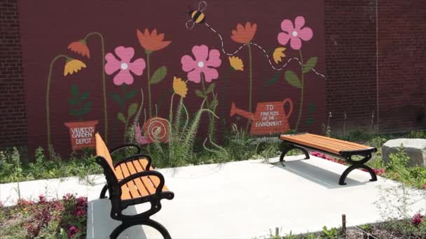後ろのレンガの壁にピンクの花の壁が付いている舗装のセメントで互いに直面する2つのベンチ — ストック動画
