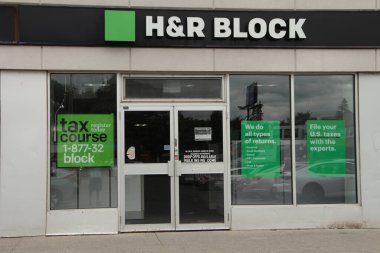 Küçük mağazanın ön girişinde h ve r blok logosu, alçak açıdan çekilmiş arka planda gökyüzü, yeşil beyaz ve siyah