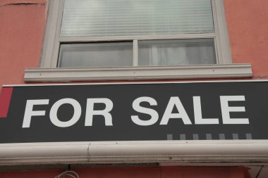 Mağazanın önündeki pencerenin altındaki satılık tabela için, siyah yatay tabela arkaplanda beyaz büyük harflerle başlık, beyaz pencereli turuncu bina duvarı, kapat