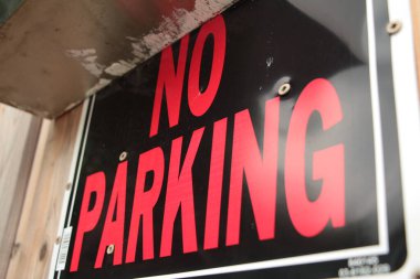 Ahşap çitlere tutturulmuş park yeri dikdörtgeni işareti yok. Siyah arka planda beyaz kenarlı kırmızı büyük harfler var.