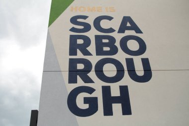 Scarborough metin başlığı binanın yan tarafında dört satır üzerine yazılmış orta çerçeve siyah büyük harflerle beyaz arkaplan sağ arka plan ekranında gökyüzü sol ekran