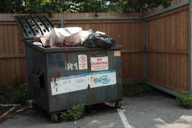 Park yerindeki aşırı dolu çöp konteynırının etrafı ahşap çitlerle çevrili.