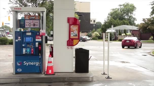Essoのガソリンスタンドのポンプ 木や背後にある空 濡れた地面 交通通過 — ストック動画