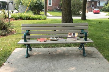 Park parkette bankında bir sürü kitap var ve insanlar yok, yeşil kolluklar ve bacaklar, çimento döşeme üzerinde, ağaçlar ve yerleşim caddesi arkasında, dümdüz vurulmuş.