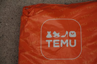 Temu turuncu dikdörtgen çanta paketi üzerinde logo var. Kaldırım çimento üzerinde duruyor. Sol çerçeve, logo sağ altta.