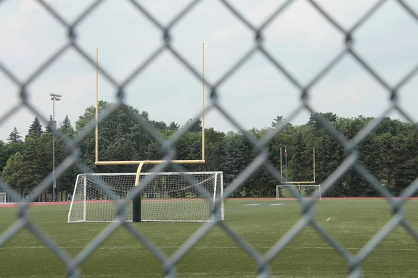 empty outdoor stadium with soccer nets yellow football goal posts and track around, shot through silver diamond fence
