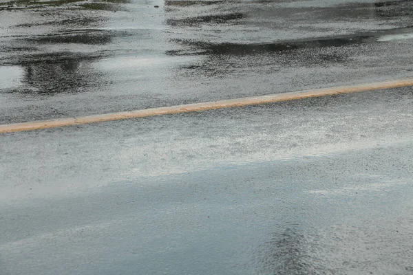 wet road with rain falling on it puddles with yellow line in the middle