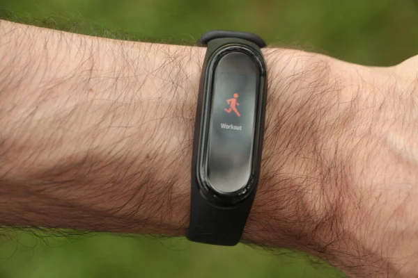 black fitness tracker wristwatch on adult male wrist with picture of orange person running with caption writing text workout beneath it and grass underneath
