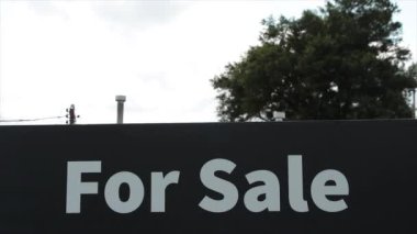 Siyah arkaplanda beyaz kalın harflerle satılık tabela ve rüzgarda esen arka planda ağaç.