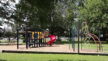 Boş çocuklar için çocuk parkı çocuk parkı. Ağaçlı ve yollu araç trafiği arka planda, kırmızı kaydırak, mavi sarı turuncu