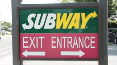 Metro sandviçi giriş çıkış tabelasında her yeri işaret eden oklar, giriş yapan araba ve arka plandan geçen trafik sıcak yaz gününde her yönden sola doğru.