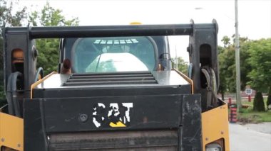 Tırtıl makinesinin arkasında solmuş kedi logosu vardı. Yoldaki Machiney 'in arkasında beyaz sarı bir logo. Yoldan geçen yayalar vardı.