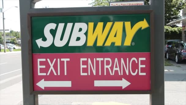 地下鉄サンドイッチ レストランの入口の出口に矢印が付いている印 熱い夏の日の左の左のバックグラウンドで道を通る車の出口および交通 — ストック動画