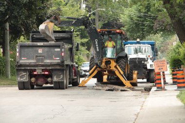 Kazıcı beton kırıcı kepçeci kepçeci kaya matkabı makinası çöplük kamyonuna beton dökerek sokak onarımını yapıyor.