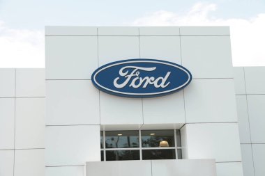 Arka planda ve aşağıda gökyüzü ve penceresi olan beyaz mağaza girişinde Ford bayii logosu, orta çekim