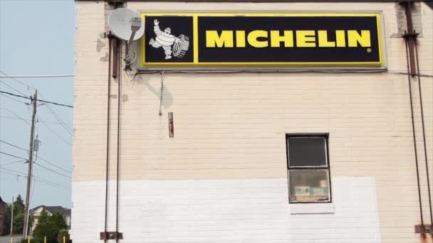 米其林标志水平矩形标志与白色轮胎吉祥物旁边的建筑存储墙 汽车交通通过道路的左边 黄色文字文字的黑色背景 — 图库视频影像