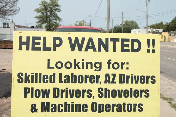 help wanted looking for skilled laborer az drivers plow drivers shovelers and machine operators sign with road and sidewalk in background, yellow sign with black writing