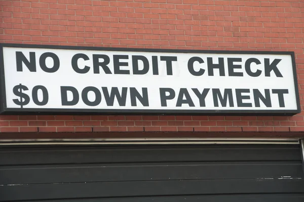 no credit check 0 zero dollar down payment sign outside on wall above garage, black writing on white background, close up