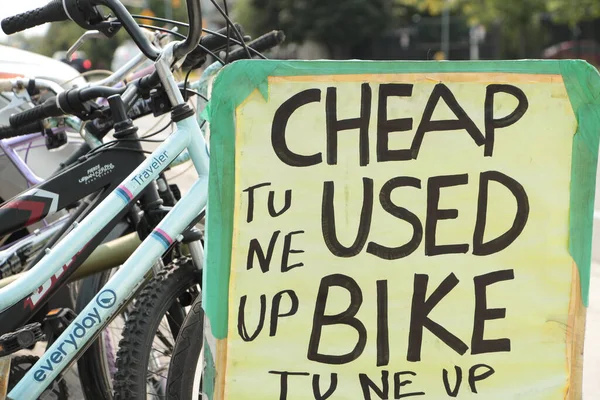 cheap used bike tune up rectangle handwritten in black marker sign with parked bicycles bikes behind it, close up
