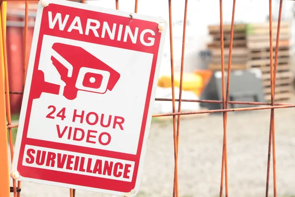 24時間ビデオ監視サイン オレンジロックされたゲート コンテナビンズスキッドパレット付きダートヤード駐車場 クローズアップ 赤と白 — ストック写真