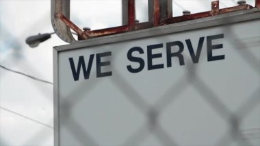 Biz manşet metni yazıyoruz. Metal direklere yatay tabela yazıyoruz. Paslı, beyaz üzerine siyah, önünde gümüş elmas çitlerle kapatıyoruz.