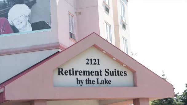 退休套房湖边标志天窗顶篷雨篷文字说明退休家庭大楼浅粉色和白色 后面阳光明媚 — 图库视频影像
