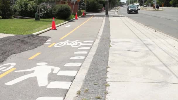 自転車の自転車の歩行者道の隣には 黄色いラインとパイロン 車の車の車の交通が通過する舗装セメントの人のステンシルアウトラインと自転車のイラストがあります — ストック動画