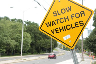 Yol kaldırımının yanındaki sarı elmas çarpık tabela için yavaş saat, araba ile yakın