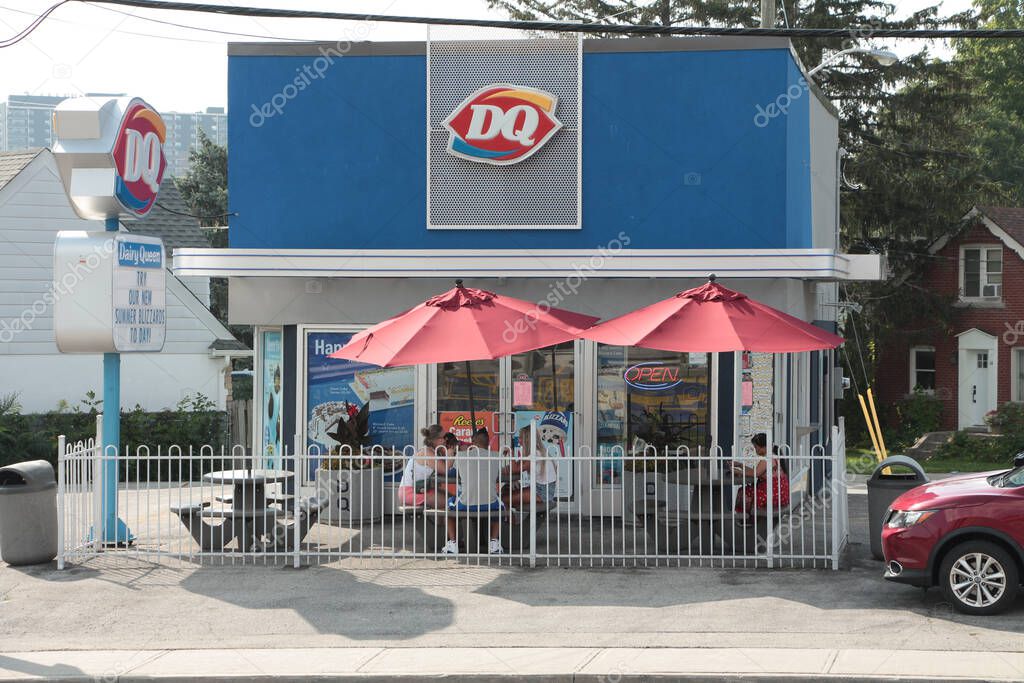 Dairy queen store restaurant with patio with umbrellas in summer with cars vehicles traffic passing on road street in front