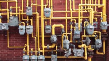 Bir sürü gri gaz sayacı bir araya toplanmış tuğla duvara monte edilmiş sarı gaz boruları tavayla tavaya doğru gökyüzüne doğru yükseliyor.